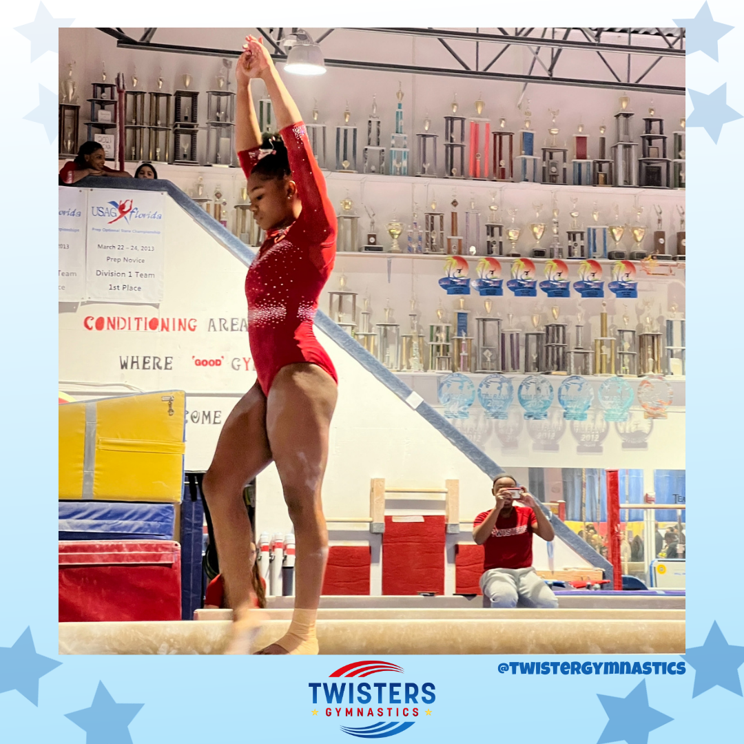 American Twisters gymnast in red leotard on beam with arms up straight